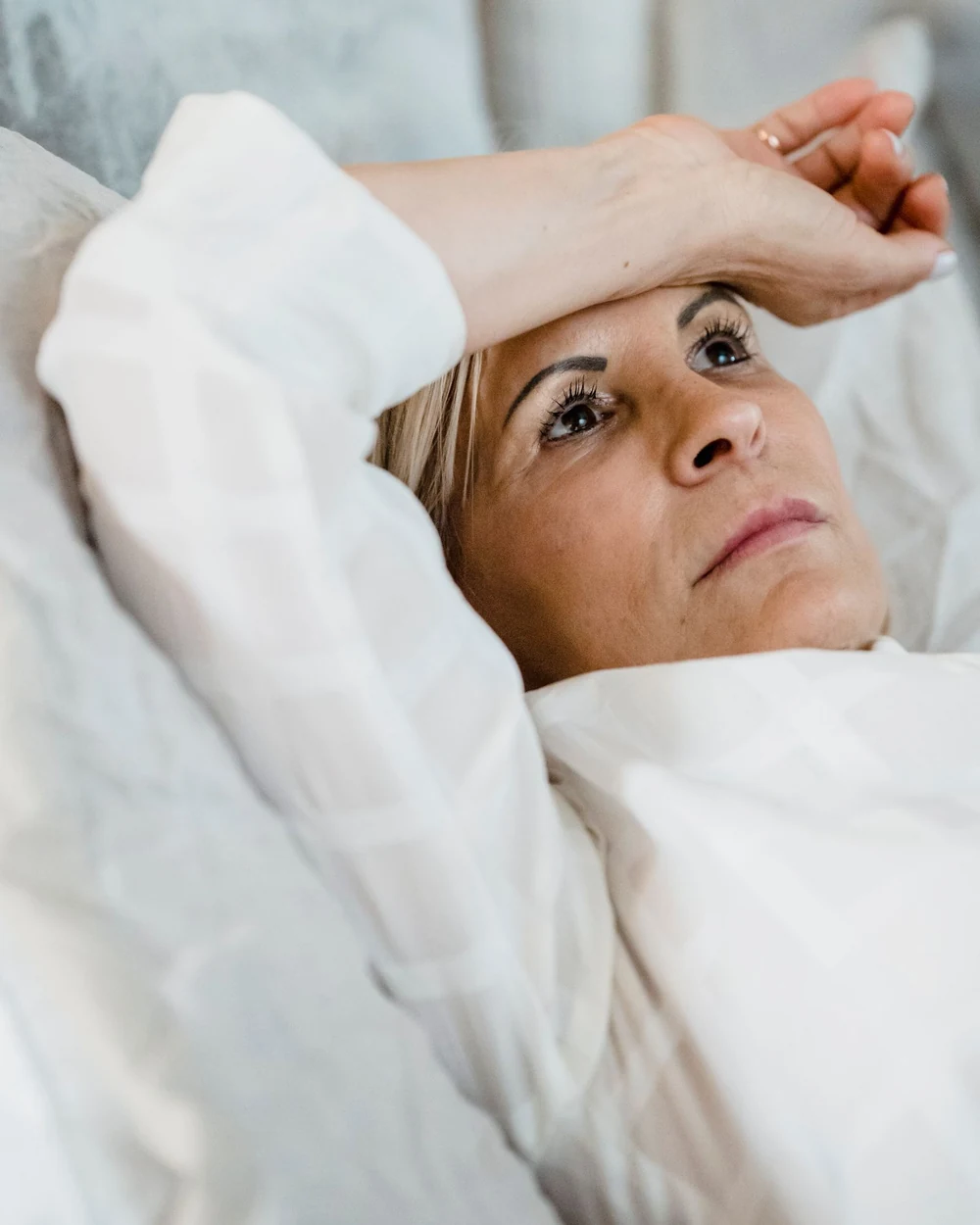Mulher madura deitada na cama, acordada de madrugada, com a mão na testa